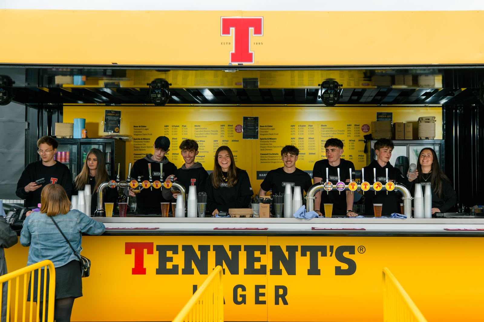 Apex staff behind a branded Tennent's bar ready to serve